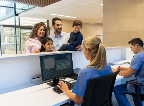 Medical front desk staff assisting family at clinic reception to improve patient experience and workflow efficiency.