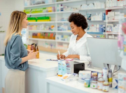Pharmacist assisting patient at retail pharmacy counter reviewing prescription and insurance claim details to prevent billing rejections and audit issues.